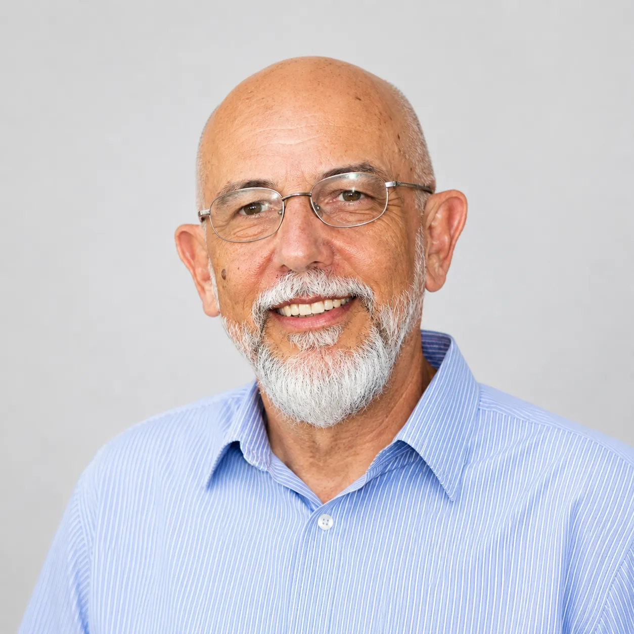 Smiling man with glasses, white beard, wearing a blue striped shirt.