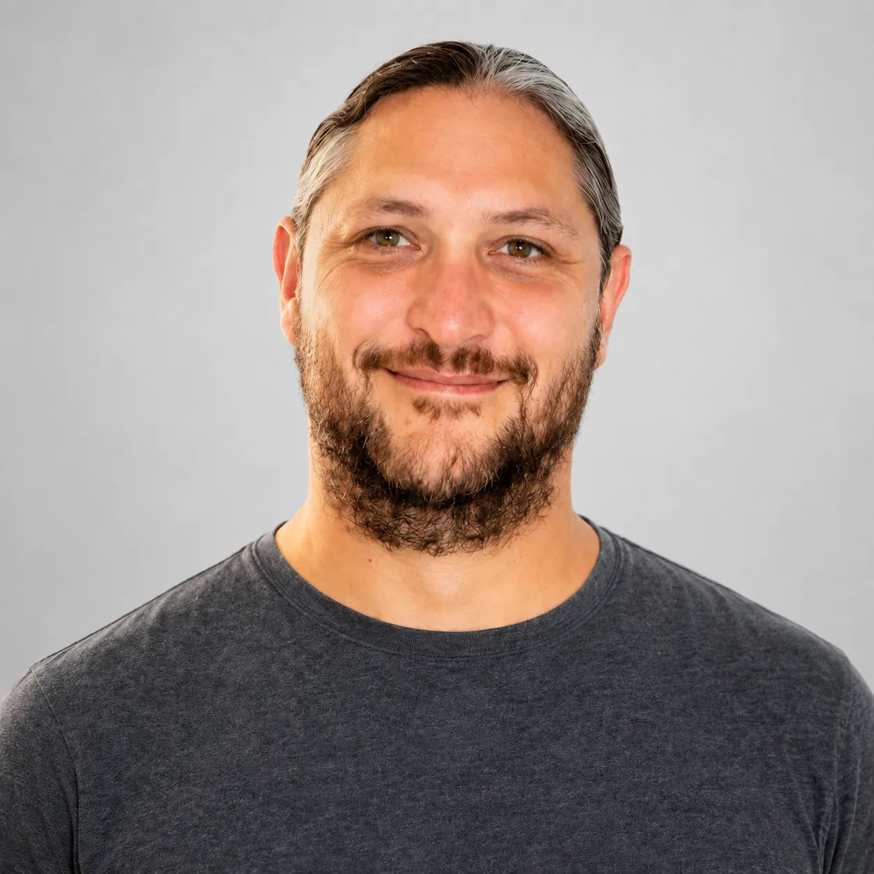 Man with light brown eyes, gray-streaked hair tied back, and a beard, wearing a dark gray shirt.