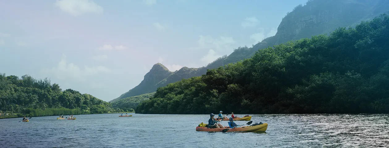 Colorful kayaks paddle a wide river between lush green mountains under a clear blue sky.