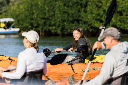 Three people kayaking on calm water near green trees, one smiling and wearing a black shirt labeled GUIDE.