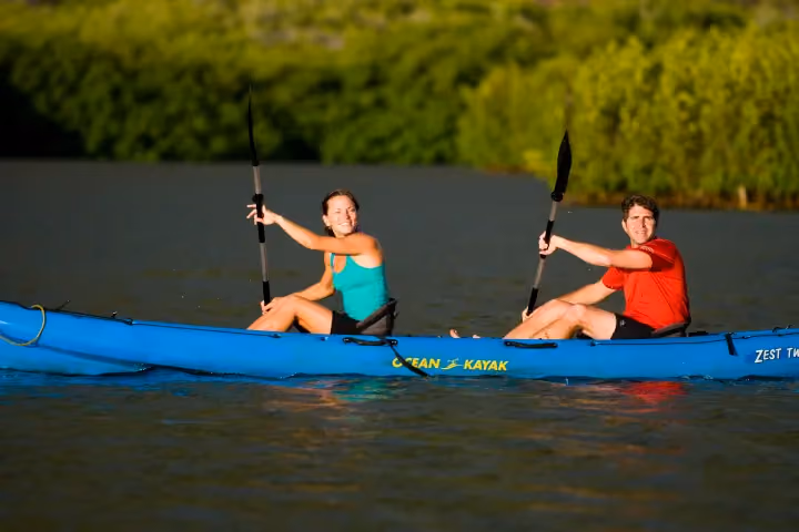 Guests kayaking on a calm Kauai river surrounded by tropical greenery.