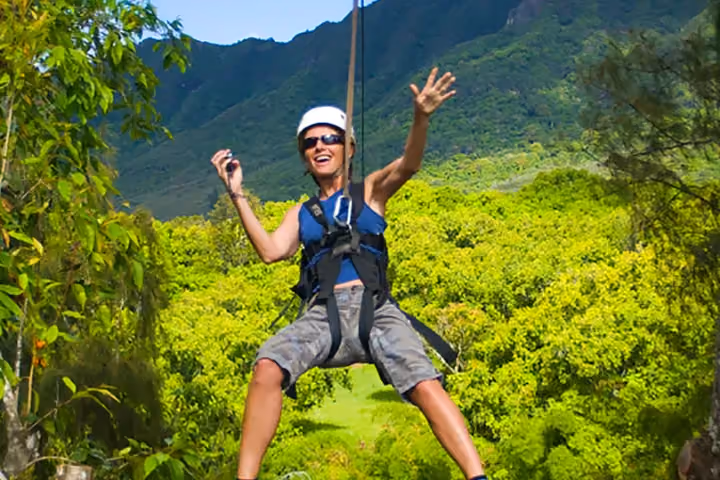 Guest ziplining over lush green Kauai forest and valleys.