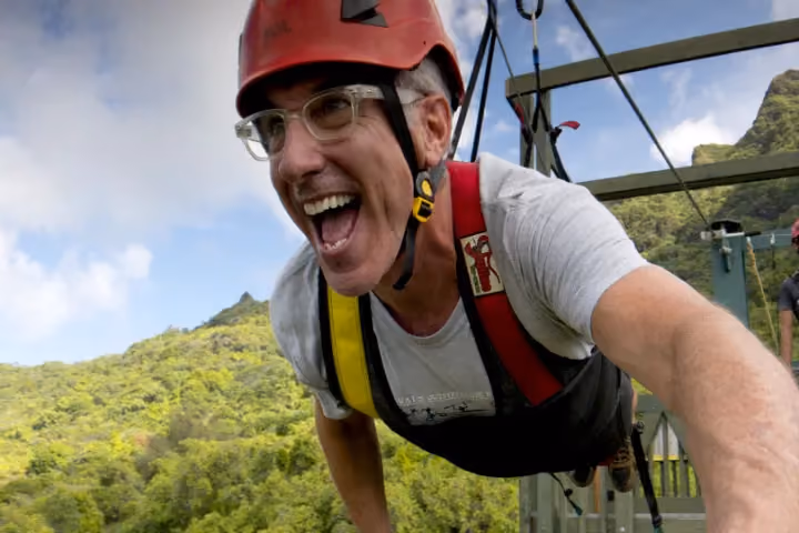 Guest ziplining over lush green Kauai forest and valleys.
