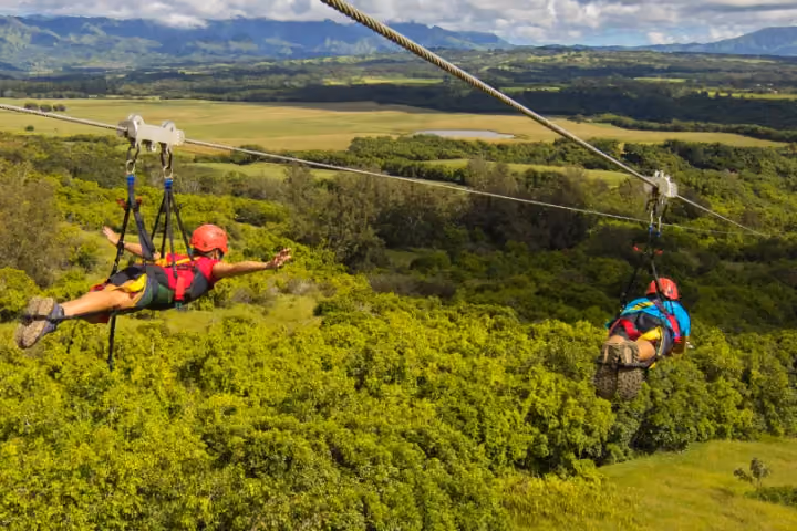 Guest ziplining over lush green Kauai forest and valleys.