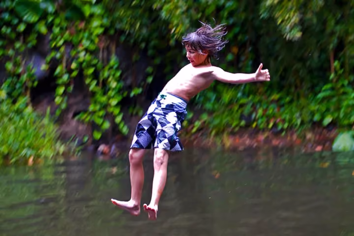 Guest splash-landing from a water zipline into a forest swimming hole.