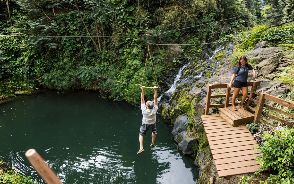 Guest ziplining over lush green Kauai forest and valleys.