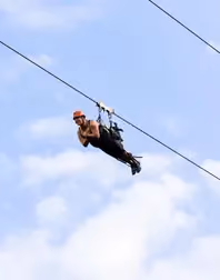 Person zip-lining through a cloudy sky, wearing safety gear and a helmet.
