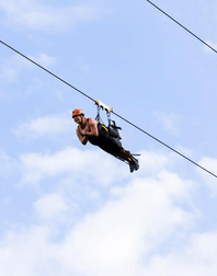 Guest ziplining against a cloudy sky in a helmet and harness