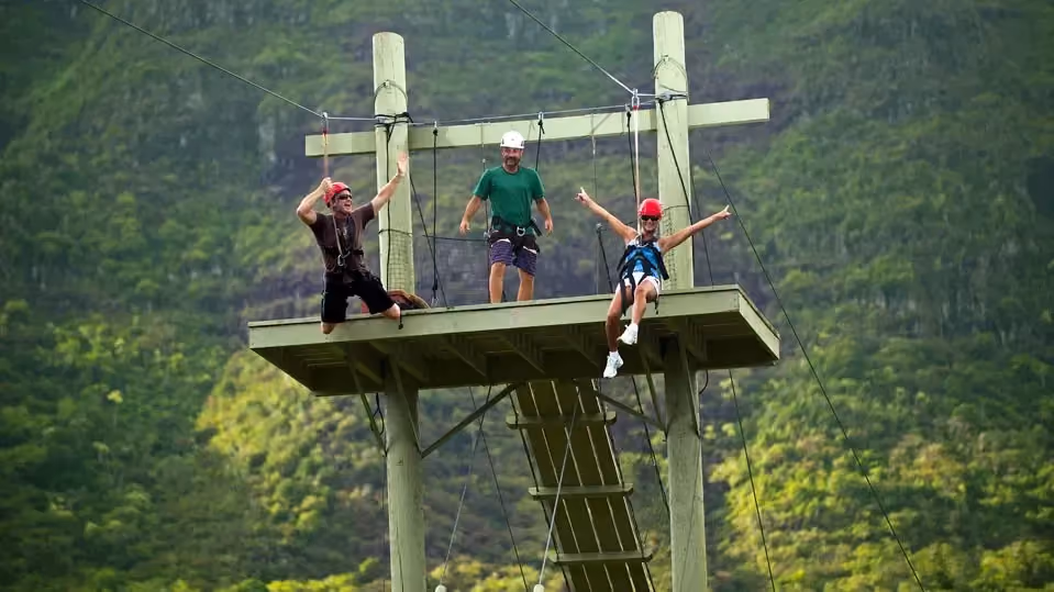 Side-by-side zipline riders flying headfirst over lush Kauaʻi landscape on the FlyLine zipline at Kīpū Ranch