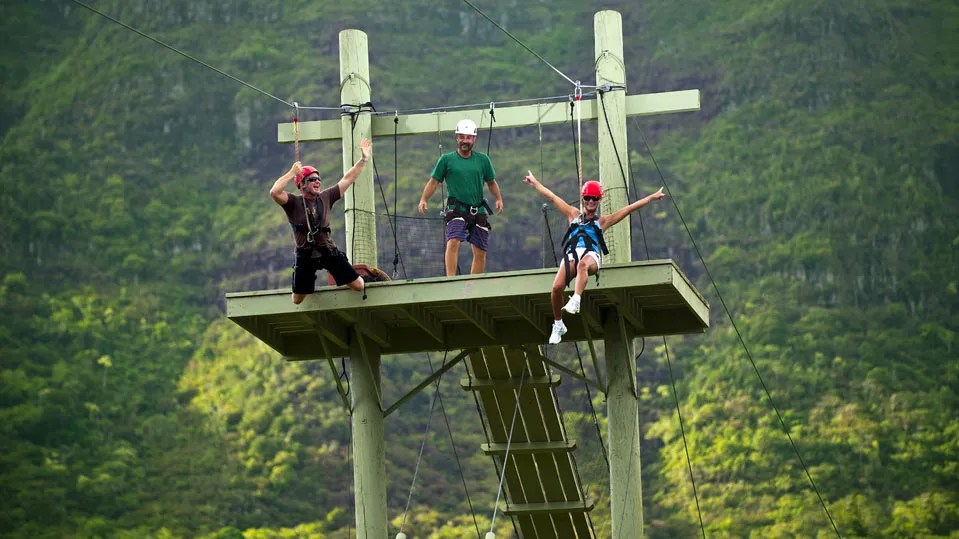 Guide and two guests on a wooden zipline launch platform at Kīpū Ranch