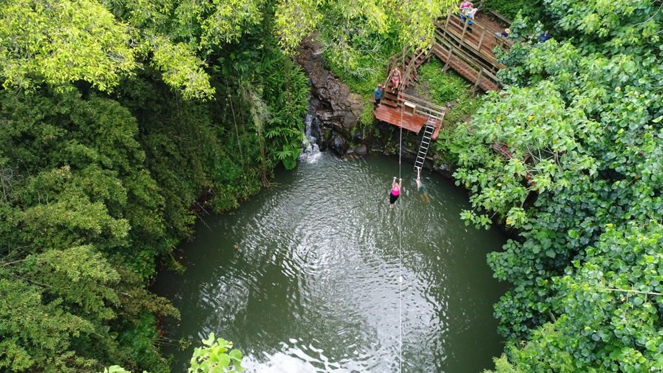 Aerial view of a guest on the water zipline above Bamboo Pool at Kīpū Ranch