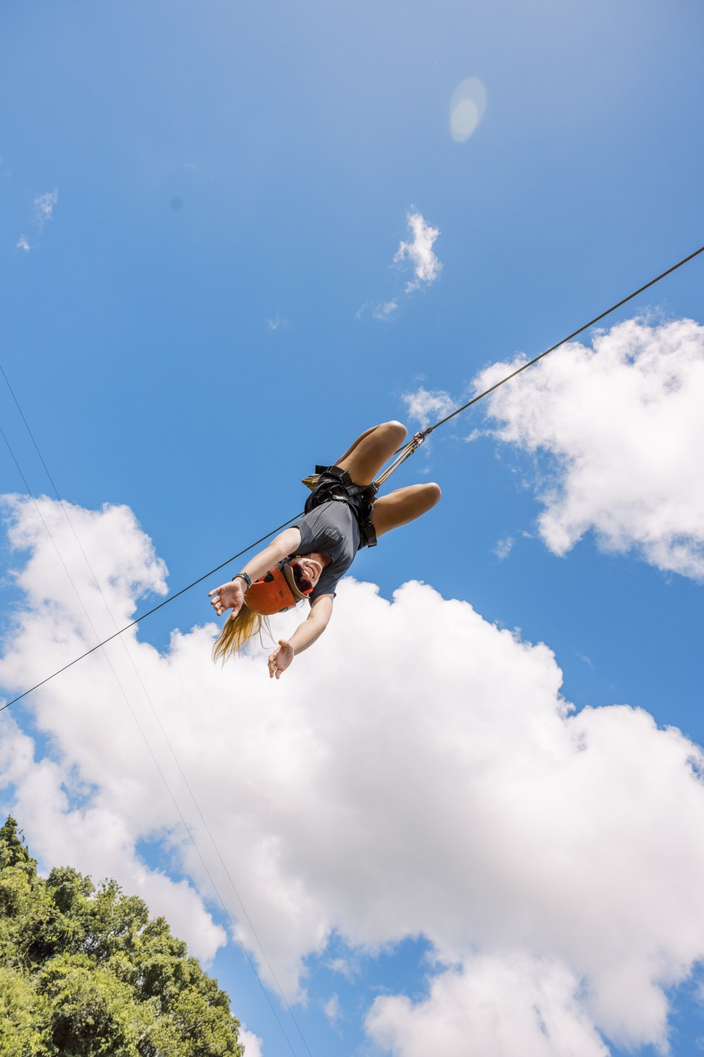 Zipliner riding upside down against a blue sky with clouds at Kīpū Ranch