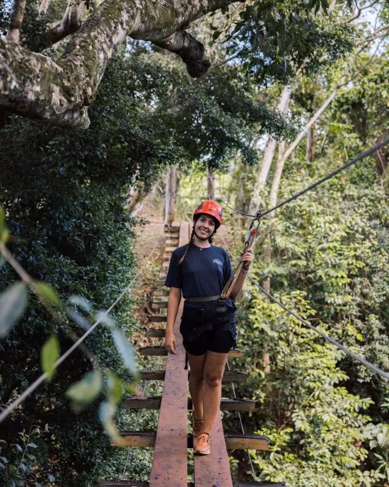 Outfitters Kauai zipline guide standing on a suspension bridge at Kipu Ranch, wearing helmet and harness surrounded by tropical forest.