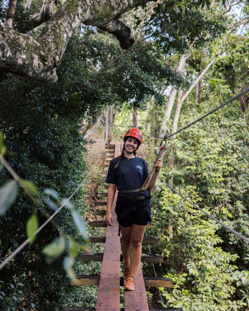 Outfitters Kauai guide in a red helmet on a suspension bridge in the trees at Kīpū Ranch