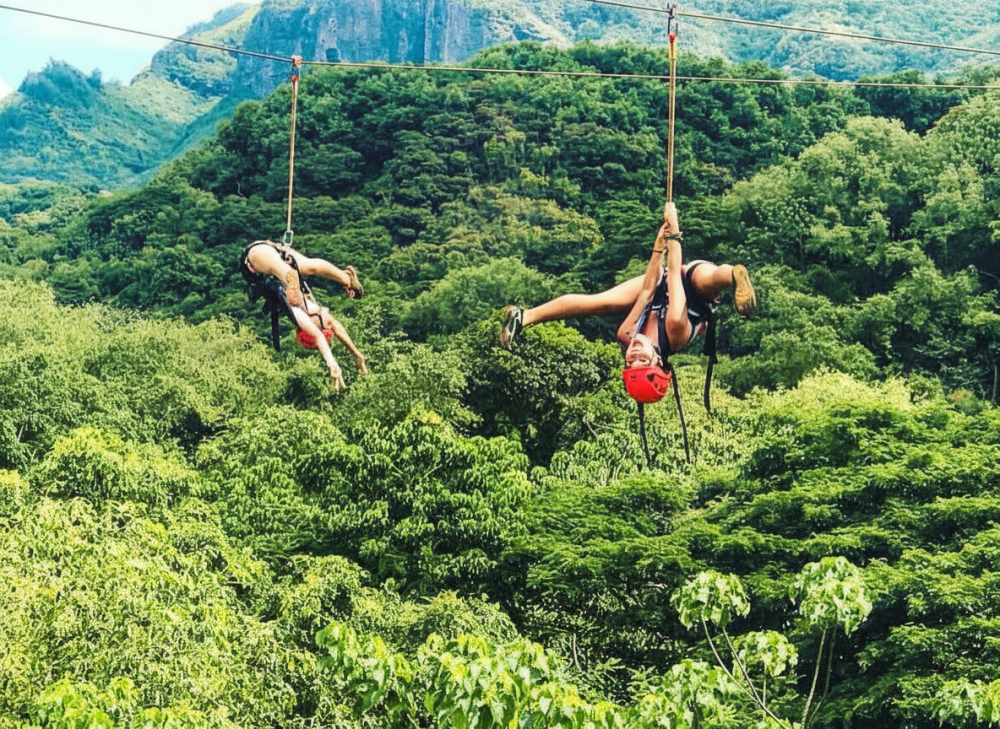 Two guests hanging upside down on parallel ziplines over the forest on the AdrenaLine tour