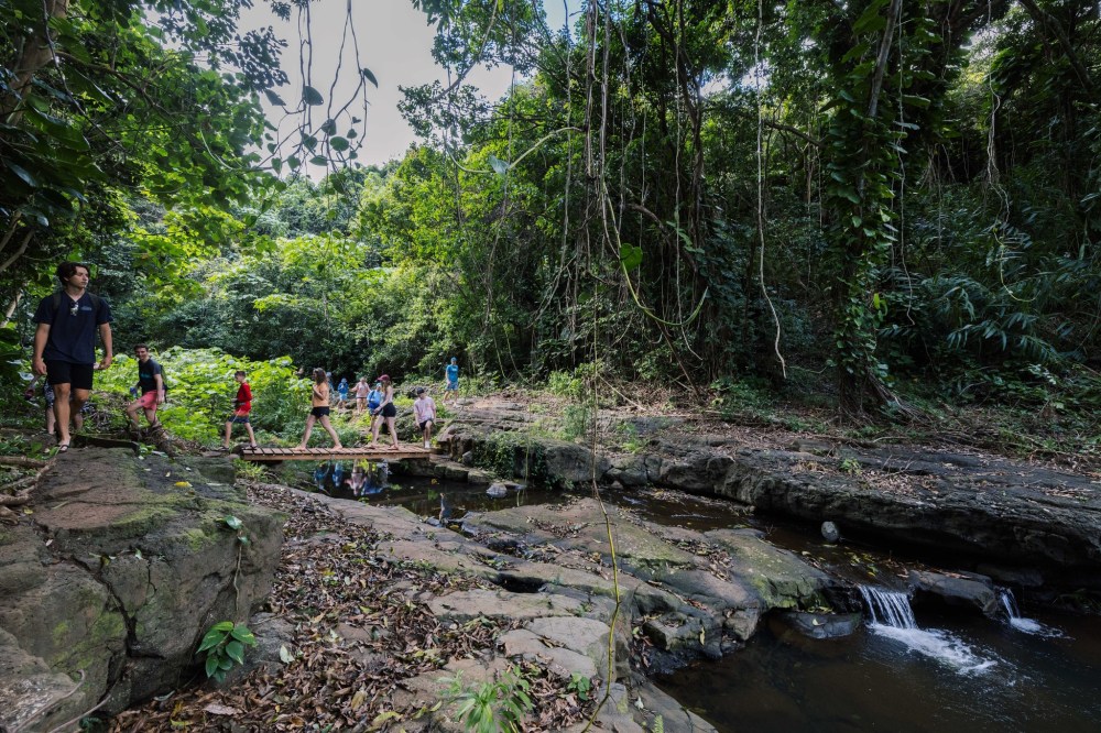 Guests crossing a rocky jungle stream on the Hidden Valley Falls hike at Kīpū Ranch