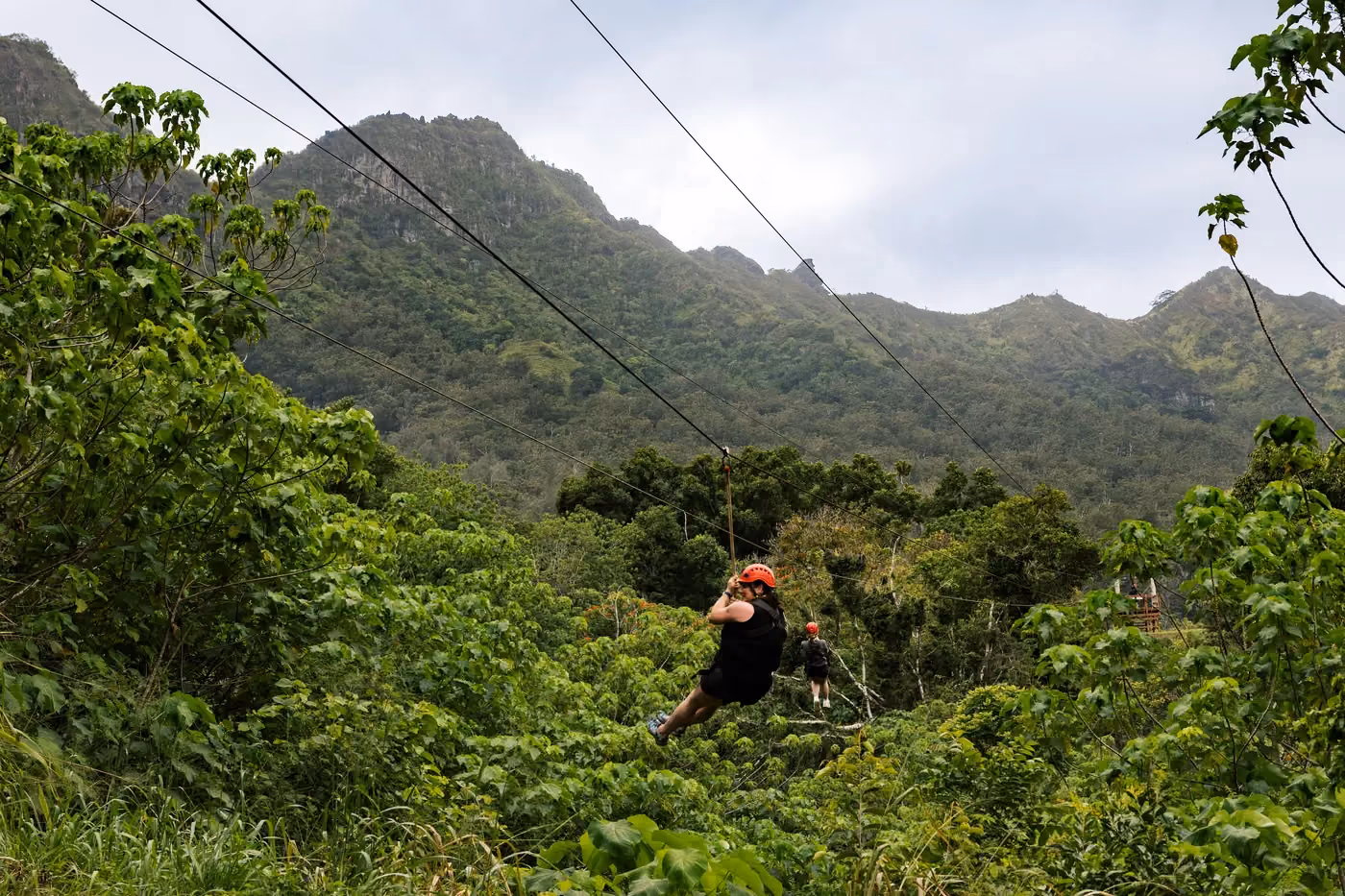 Zipline tour participant ziplining over Kauai valley with dramatic mountain backdrop