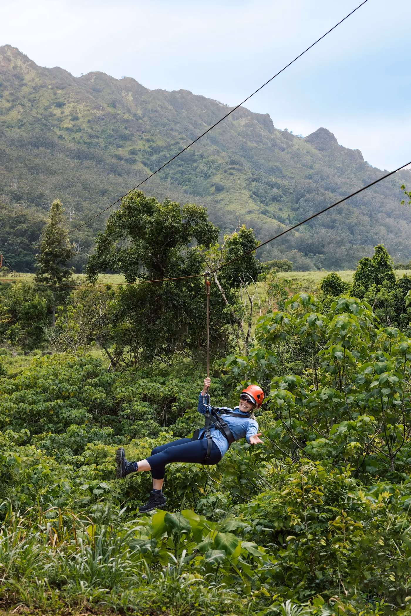 Adventure seeker zip-lining across Kauai valley with lush tropical mountain landscape