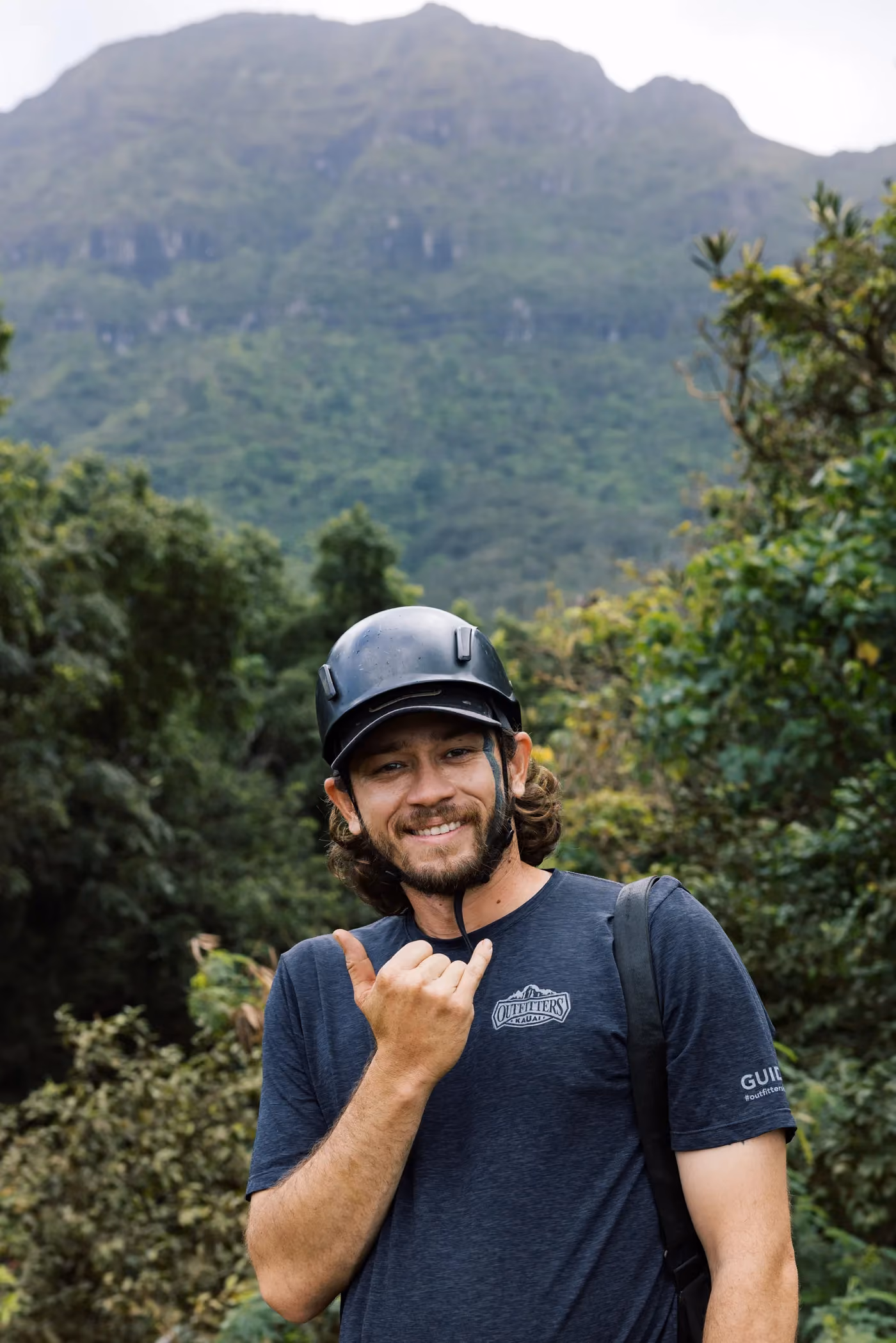 Smiling Kauai zipline tour guide posed in front of dramatic mountain landscape scenery