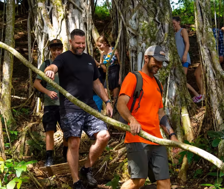 Guide leading a family through the roots of a giant banyan tree on the Kīpū Falls and Treehouse Hike