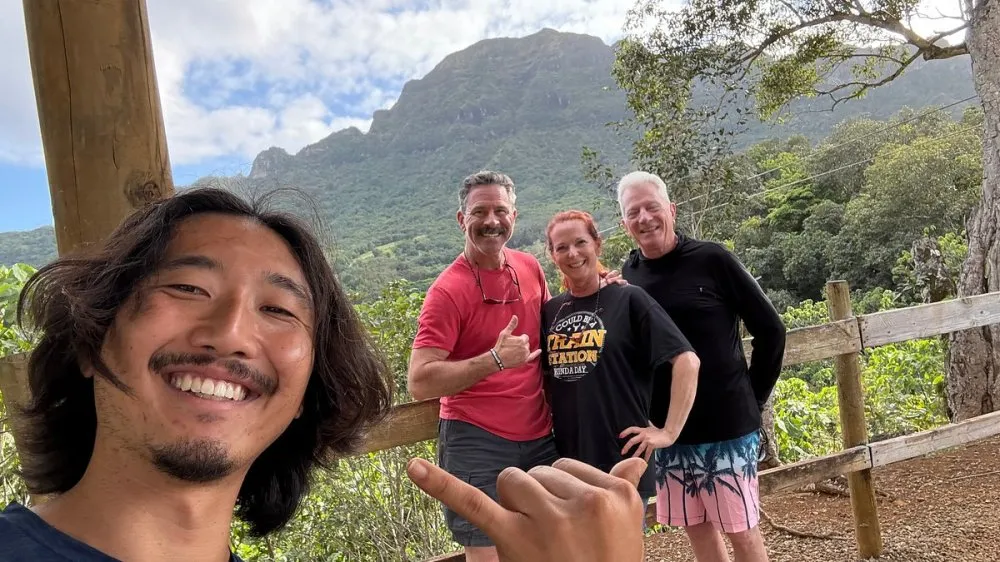 Selfie of a smiling guest with three others giving shaka below the Hāʻupu mountains