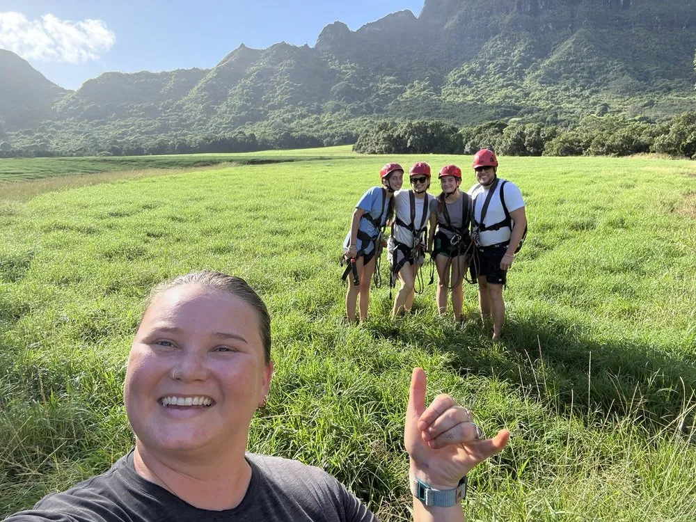 Selfie of a smiling woman with four helmeted guests in a field below the Hāʻupu mountains