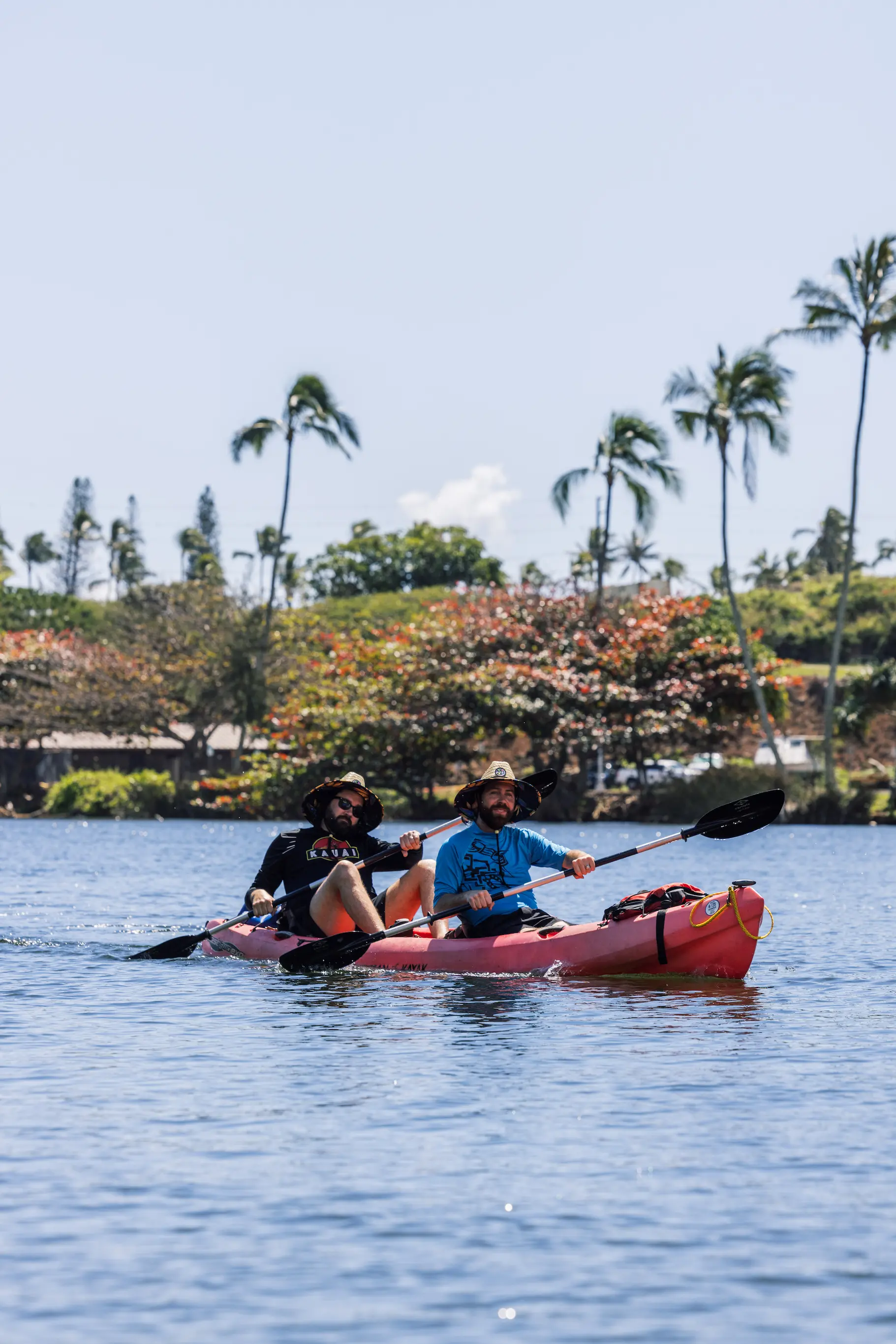 Two guests in a red tandem kayak on the Wailua River with palm trees along the shore
