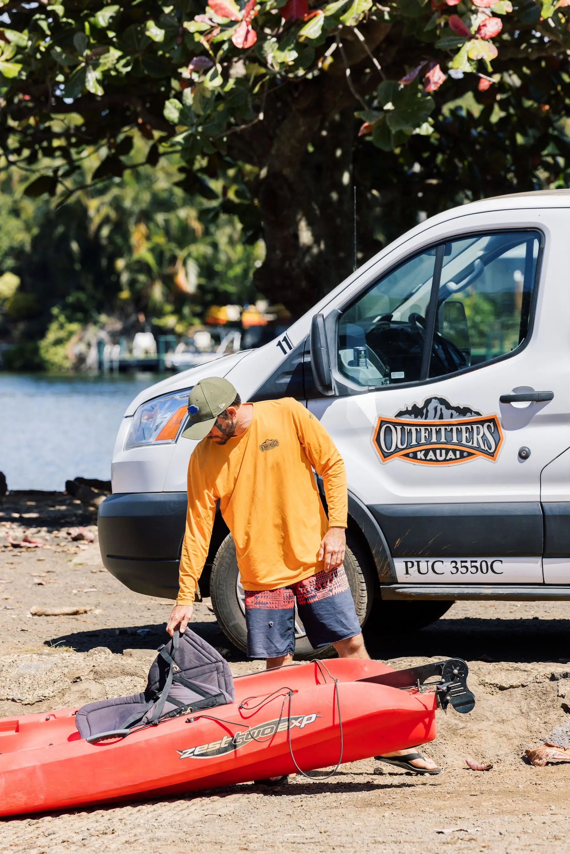 Outfitters Kauai staff loading a red kayak beside the company van at the Wailua launch