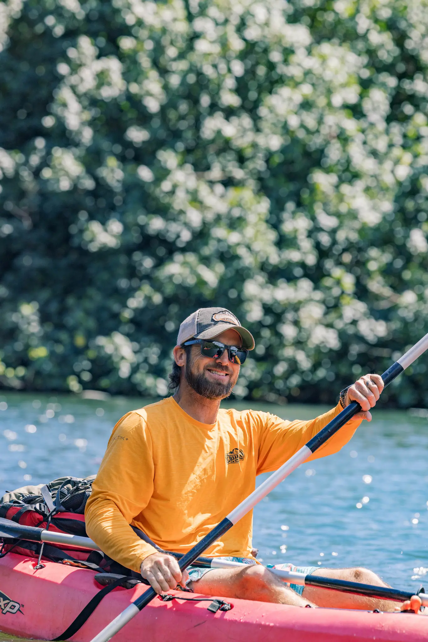 Man in an orange shirt and cap paddling a red tandem kayak on the Wailua River