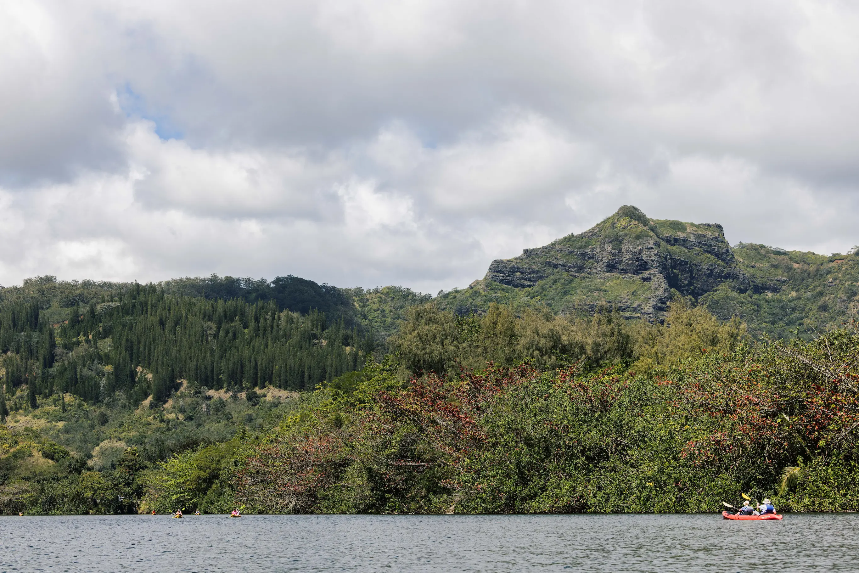 Wide view of the Wailua River with a kayak in the distance and green hills under cloudy skies