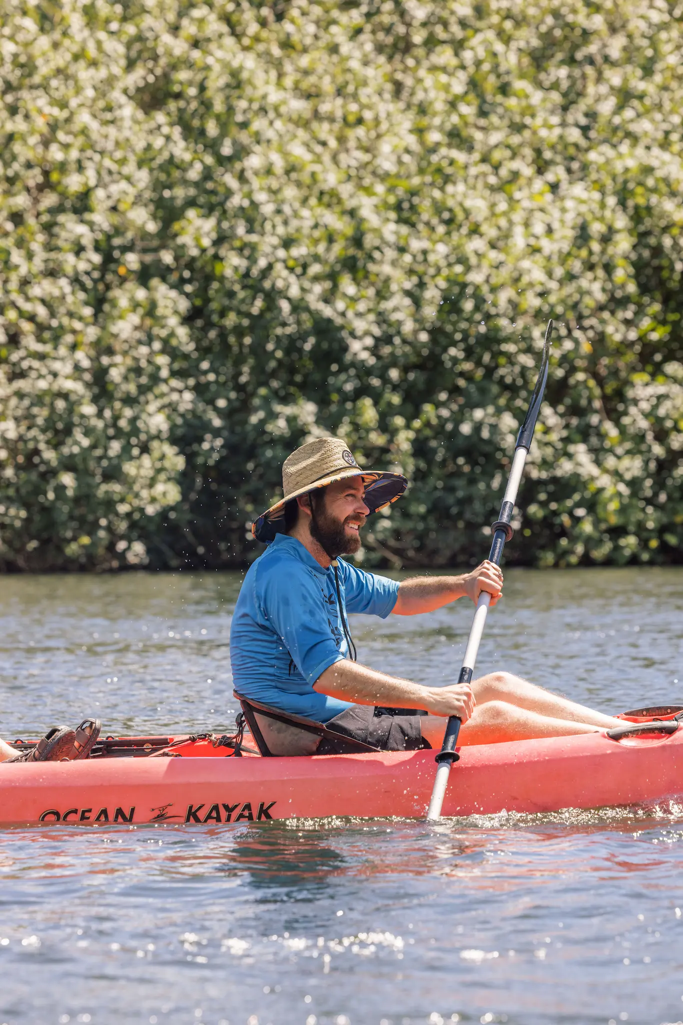 Guest in a straw hat paddling a red kayak on the Wailua River