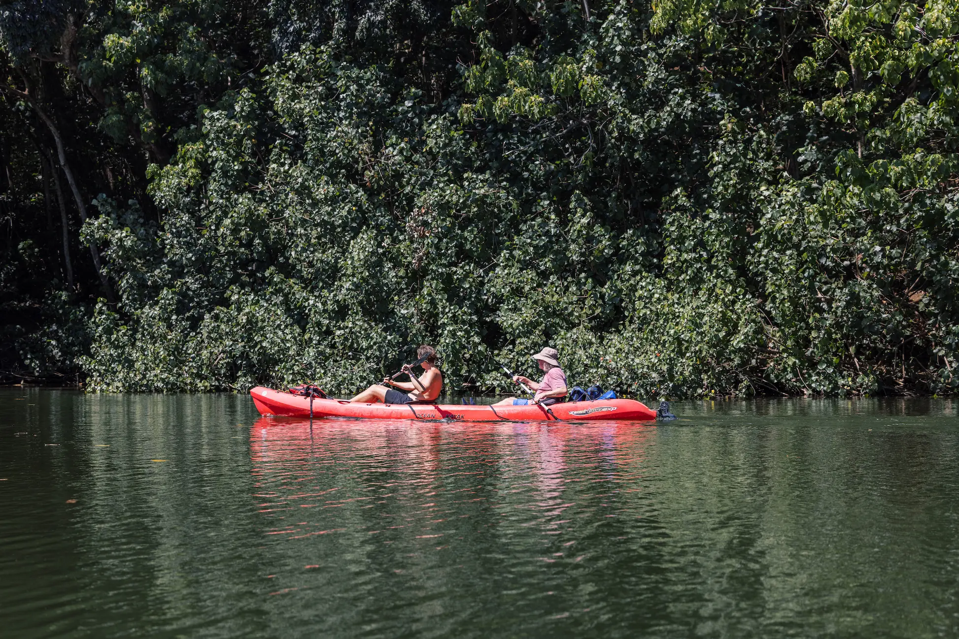 Two guests paddling a red tandem kayak on the calm Wailua River