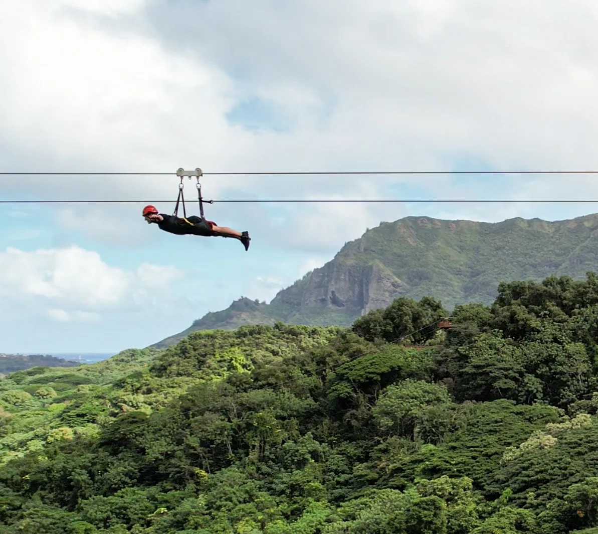 Guest flying headfirst on the FlyLine zipline above Kīpū Ranch with the Hāʻupu ridge behind