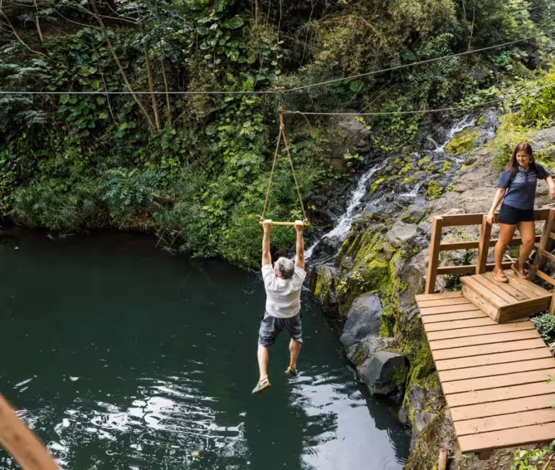 Guest swinging on the Pirate Pool rope swing above a freshwater pool on the Kīpū Safari tour