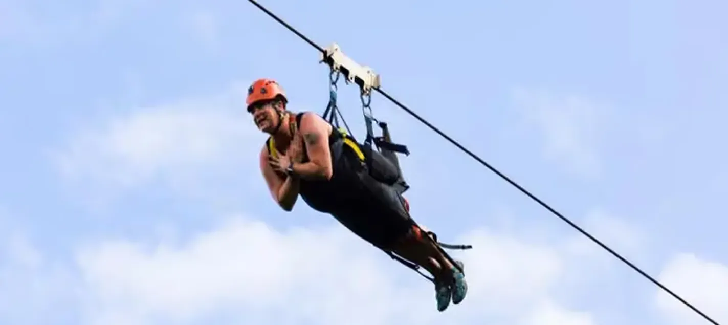 Guest in a red helmet ziplining against a blue sky at Kīpū Ranch