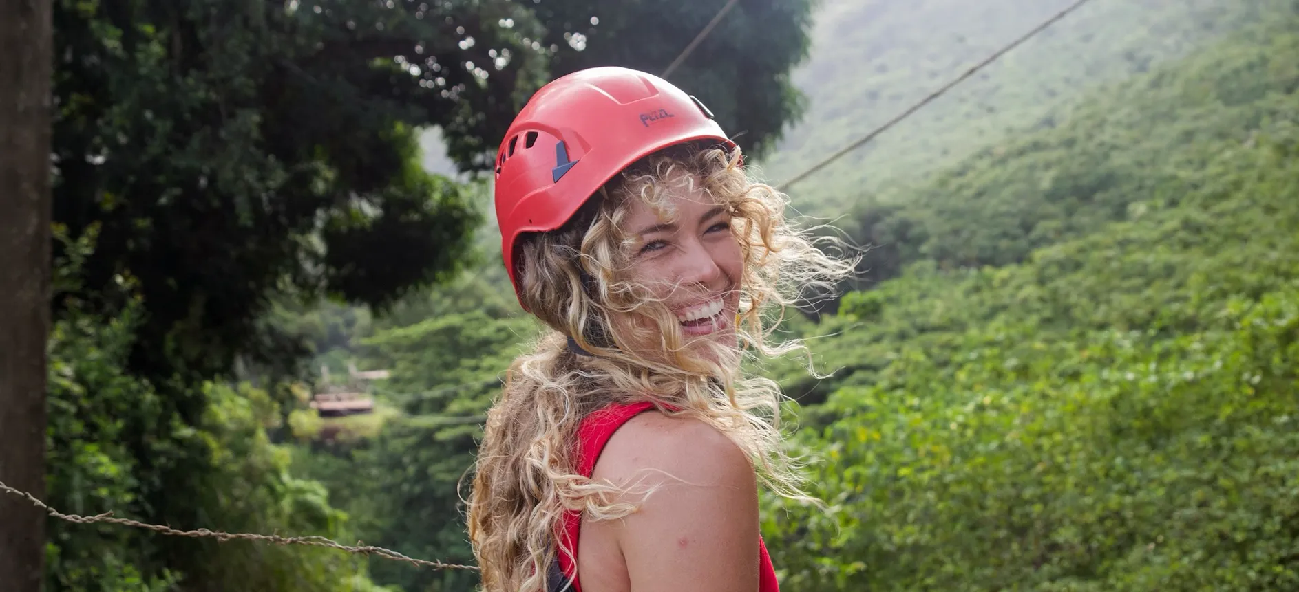 Smiling guest in a red helmet on a zipline platform with misty mountains behind