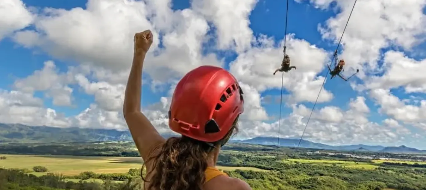 Guest cheering from the FlyLine tower as two zipliners race over Kīpū Ranch