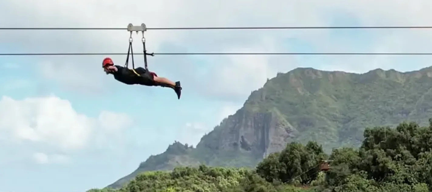 Guest flying headfirst on the FlyLine above the forest with the Hāʻupu ridge behind