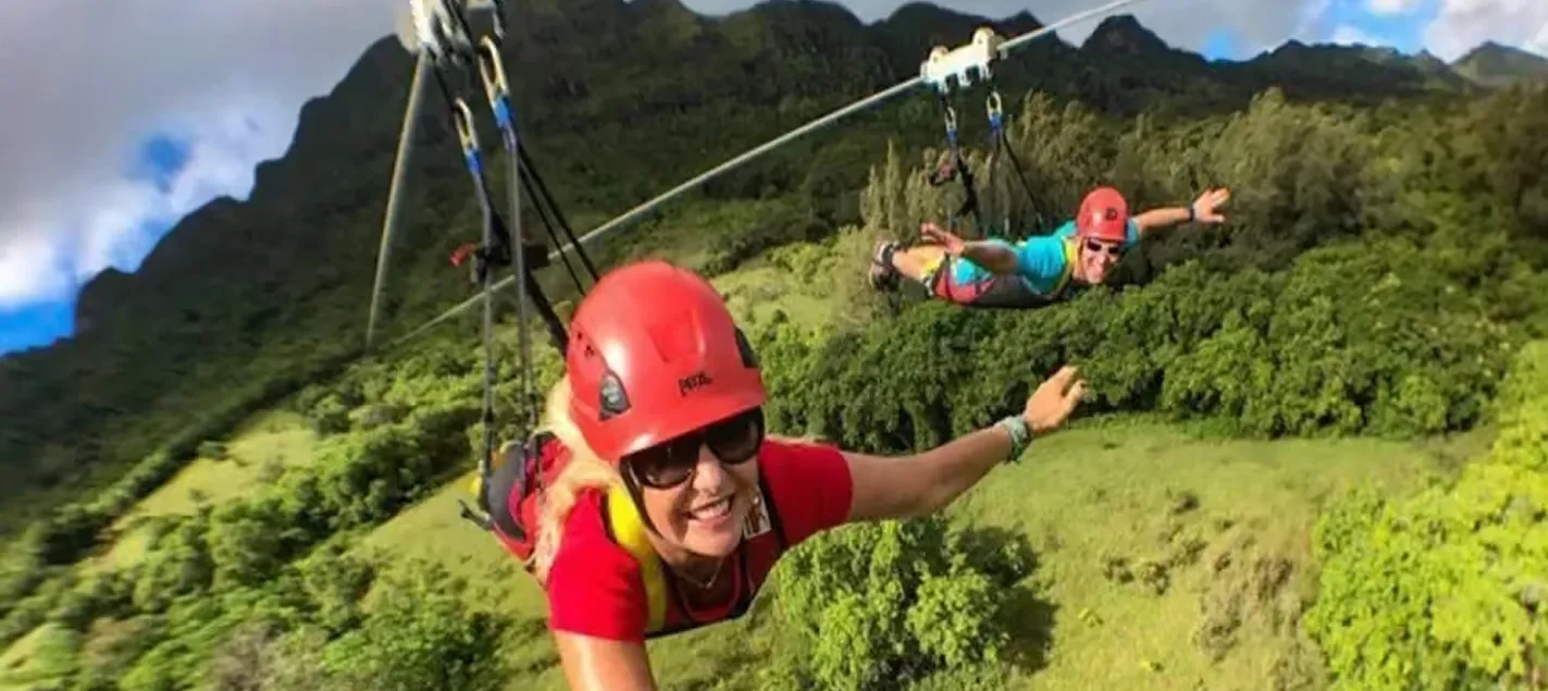 Zipliner in a red helmet flying headfirst on the FlyLine over the Kīpū Ranch valley