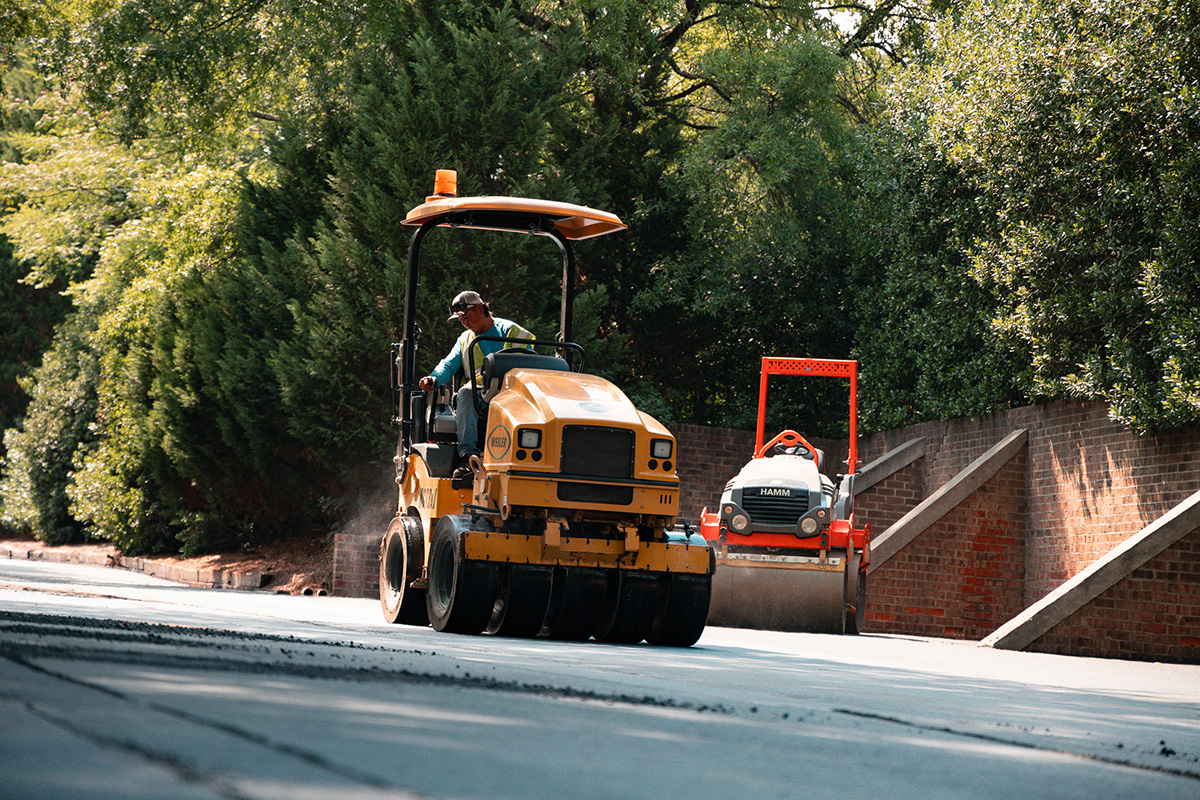 Lambeth Asphalt Services crew member operating a Weiler roller alongside a Hamm roller to compact fresh asphalt on a driveway at Friendly West in Greensboro, NC.