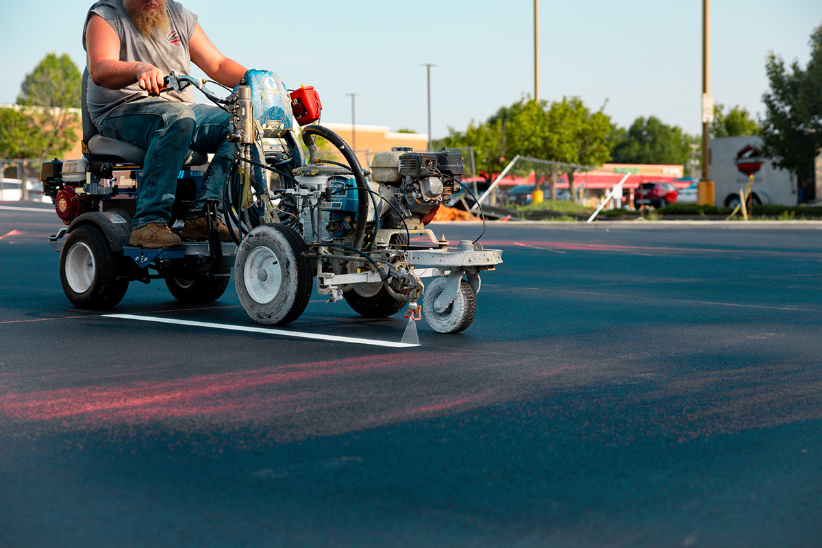 Lambeth Asphalt Services crew member operating ride-on line striper at Mavis Tire & Brakes parking lot, Greensboro NC