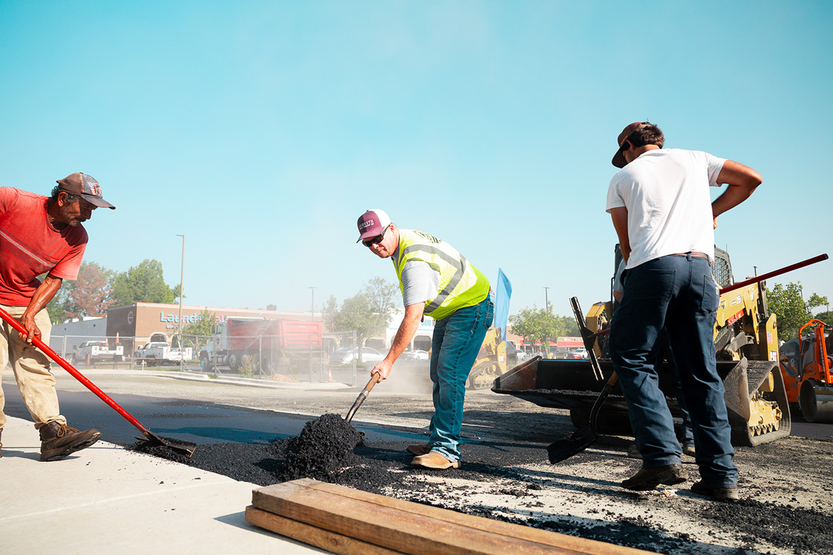Lambeth Asphalt Services crew hand-raking asphalt patch near skid steer during Mavis Tire & Brakes parking lot paving, Greensboro NC