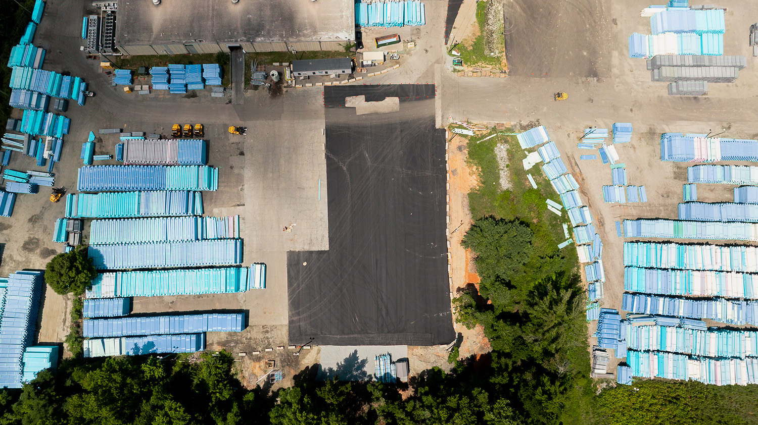 Aerial view of a freshly paved staging area at National Pipe and Plastics in Colfax, NC, fenced off amid rows of stacked PVC pipe