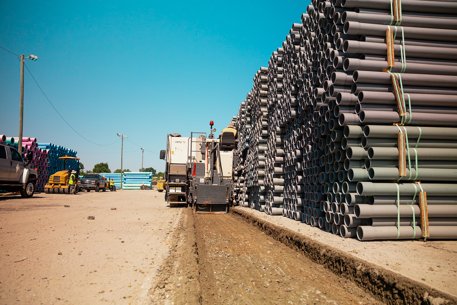 Wirtgen milling machine cutting asphalt alongside stacked PVC pipe inventory at National Pipe and Plastics, Colfax, NC