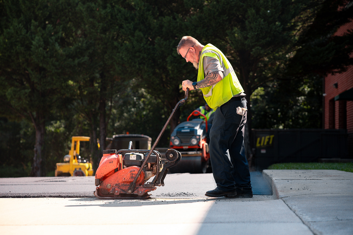 Lambeth Asphalt Services crew member operating a plate compactor along a new driveway edge at Gexpro Services, High Point, NC