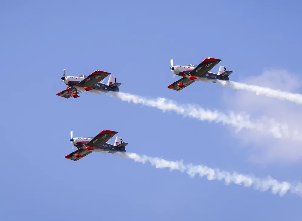 Tres avioes de acrobacia com a marca EVEO voando em formacao e deixando rastro de fumaca