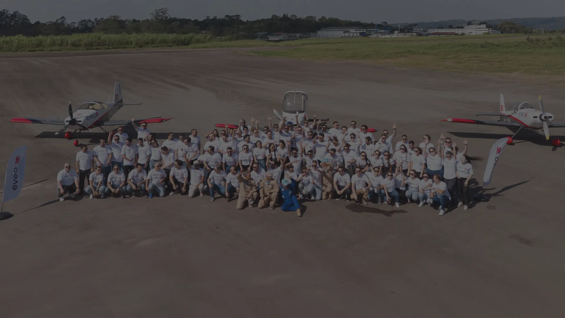 Time da EVEO reunido em uma pista de aeroporto, entre avioes de pequeno porte