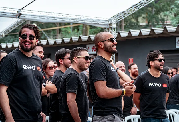 Equipe da EVEO de camiseta preta com a marca, sorrindo durante um evento ao ar livre