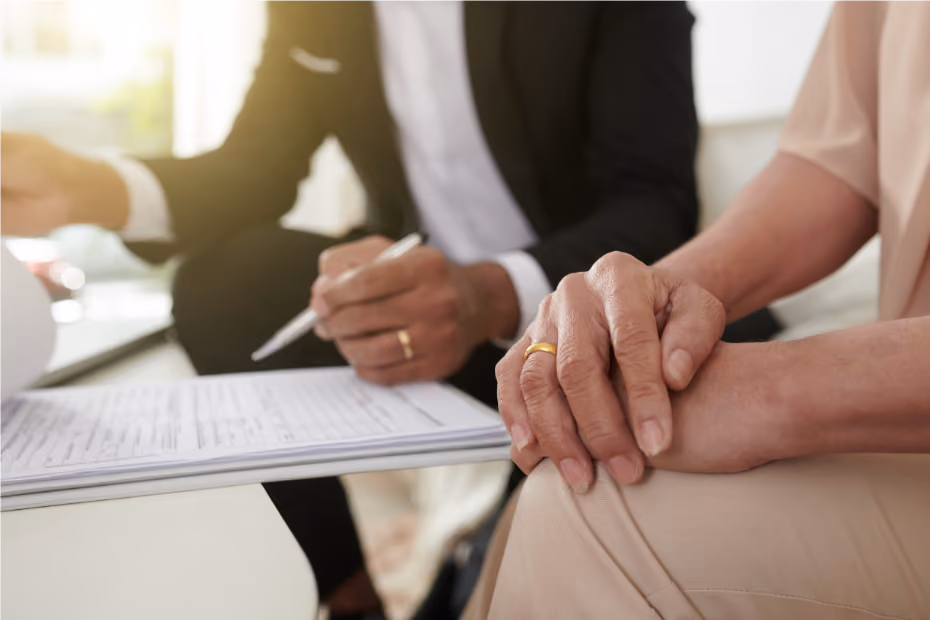Close-up of two people sitting; one writing on a clipboard, the other resting hands on their knee.