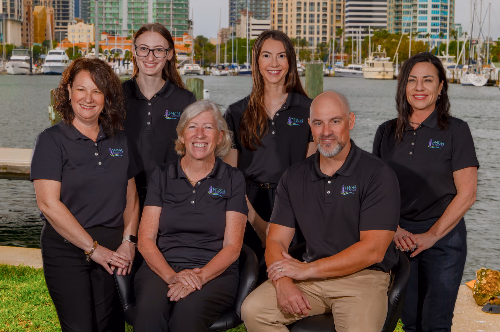 Group of HKH Elder Law Staff in black polo shirts posing by the St Petersburg marina with boats and buildings in background.